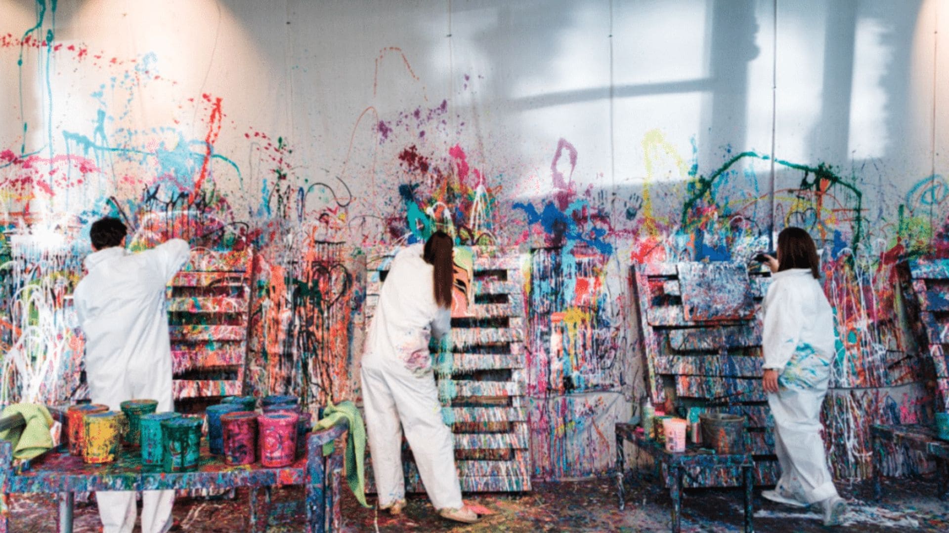 Guests painting in white coveralls at Splatter Studio, with colorful splashes covering walls, canvases, and the floor in Virginia Highland, Atlanta, GA